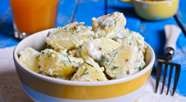 Potato salad in yellow bowl next to fork on blue wood table